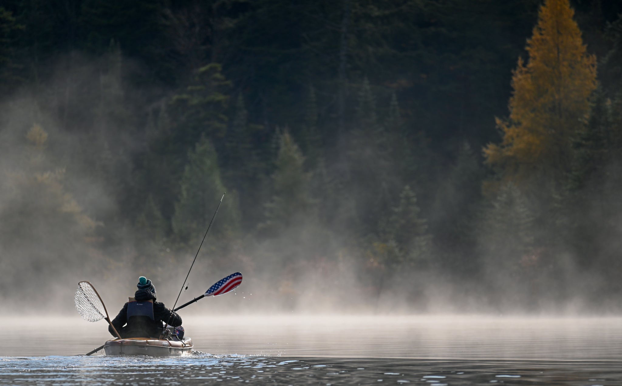 kayak fishing on a pond with fog rising off of the water.